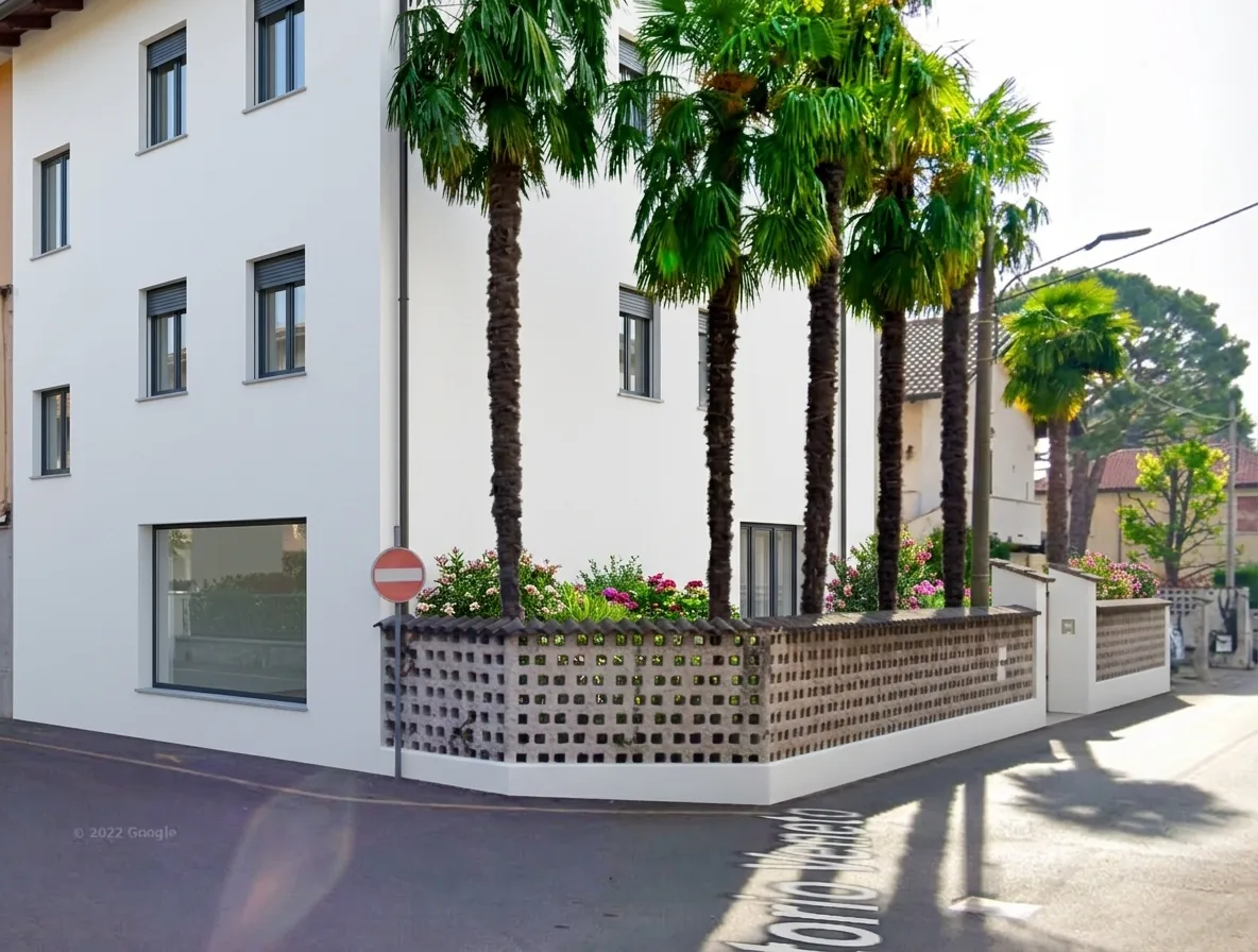Vista d'angolo della palazzina con recinzione e giardino fiorito — render di progetto